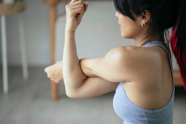 A woman is stretching her arms in the gym.