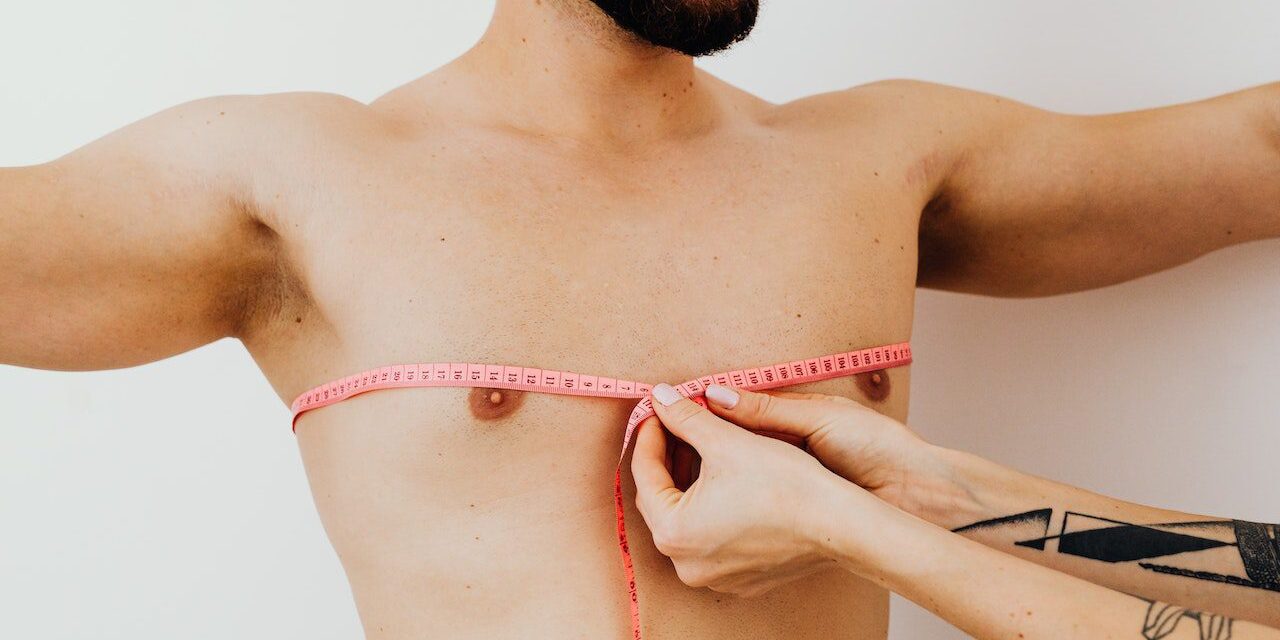 A man is measuring his chest with a tape measure.